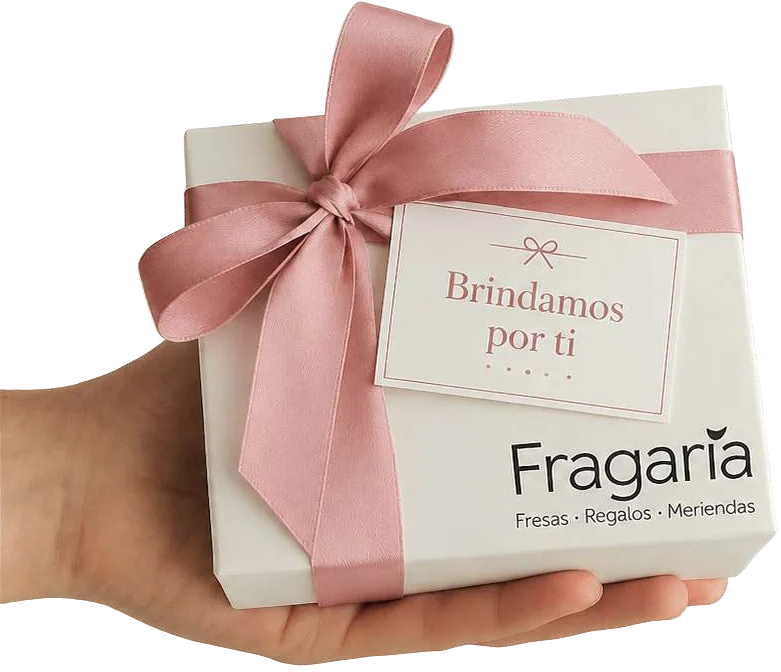 Mano sosteniendo una caja de regalo Fragaria con cinta rosa y la tarjeta “Brindamos por ti”.